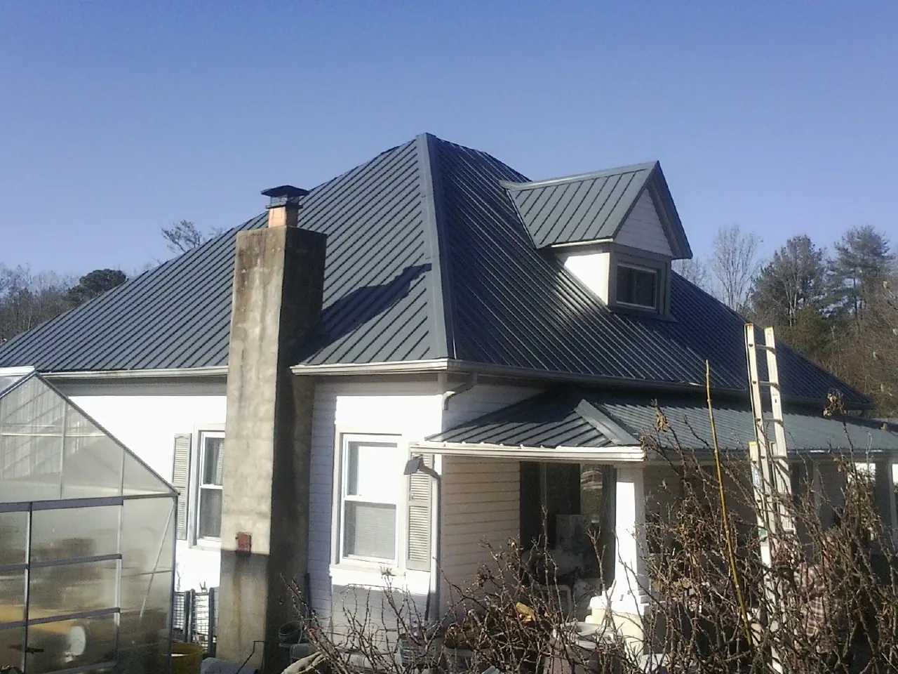 Dark blue standing seam metal roof on a white farmhouse with dormer — Slate & Tile Roof Repair by Roofing Brothers in Schaghticoke