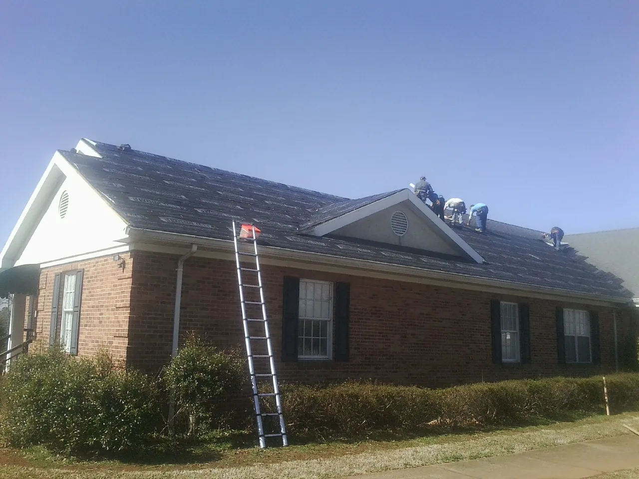 Crew tearing shingles off a brick ranch roof with a ladder set — Emergency Roof Repair work by our crew in Schaghticoke