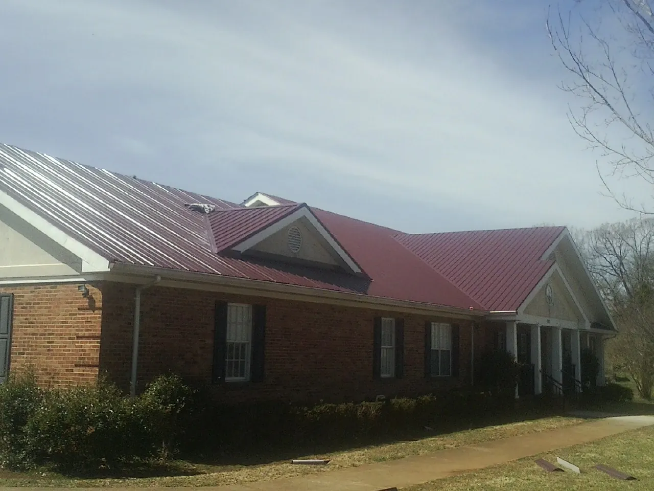 Red metal roof with gabled entries on a long brick building, from a Hail Damage Roof Repair job in Schaghticoke