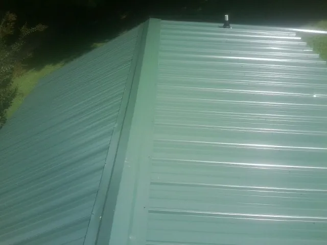 New green metal panels meeting at the ridge of a roof — Flat Roof Repair work by our crew in Schaghticoke