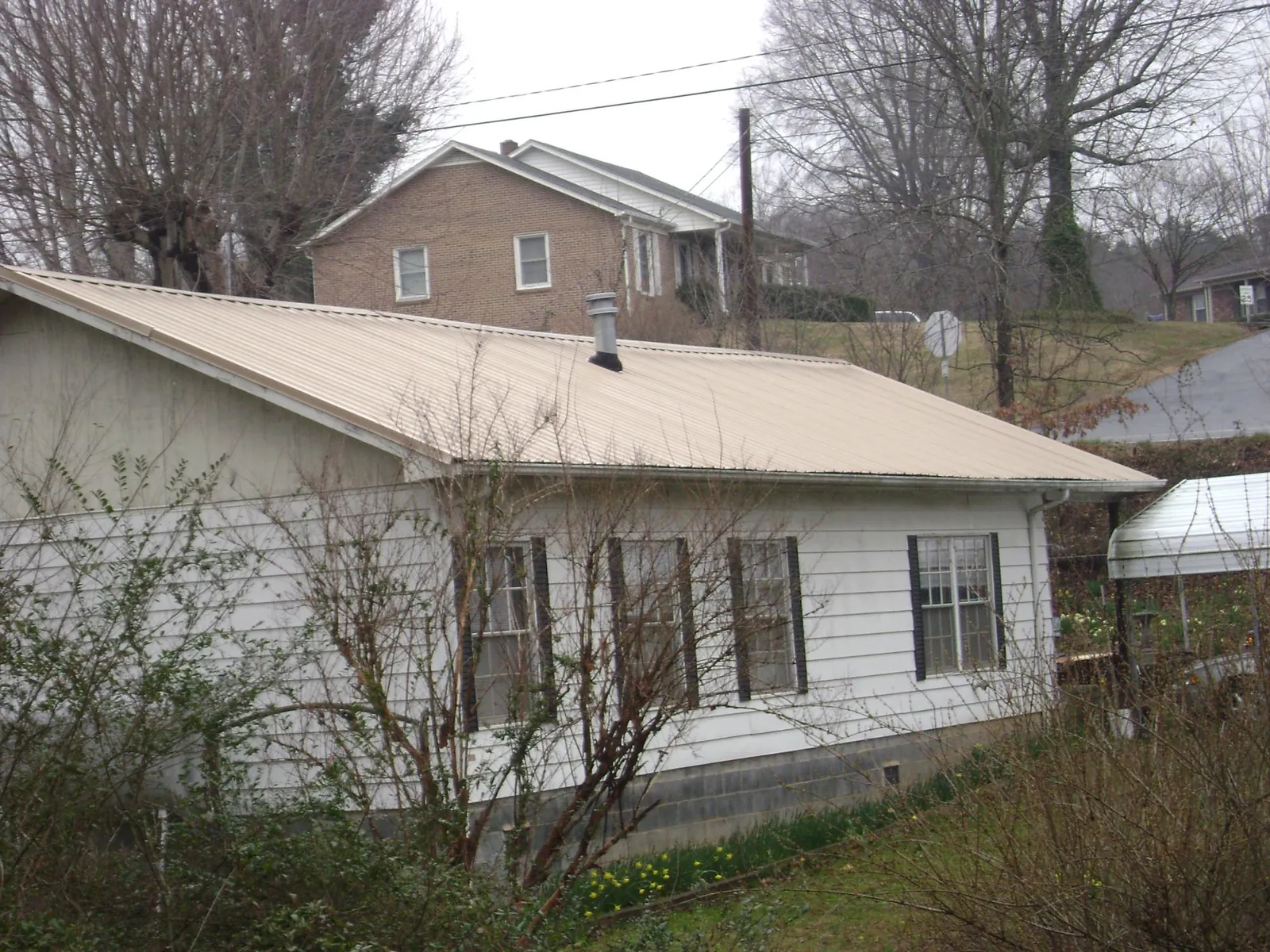 Tan metal roof on a white sided house set into a hillside — Commercial Roofing by Roofing Brothers in Schaghticoke